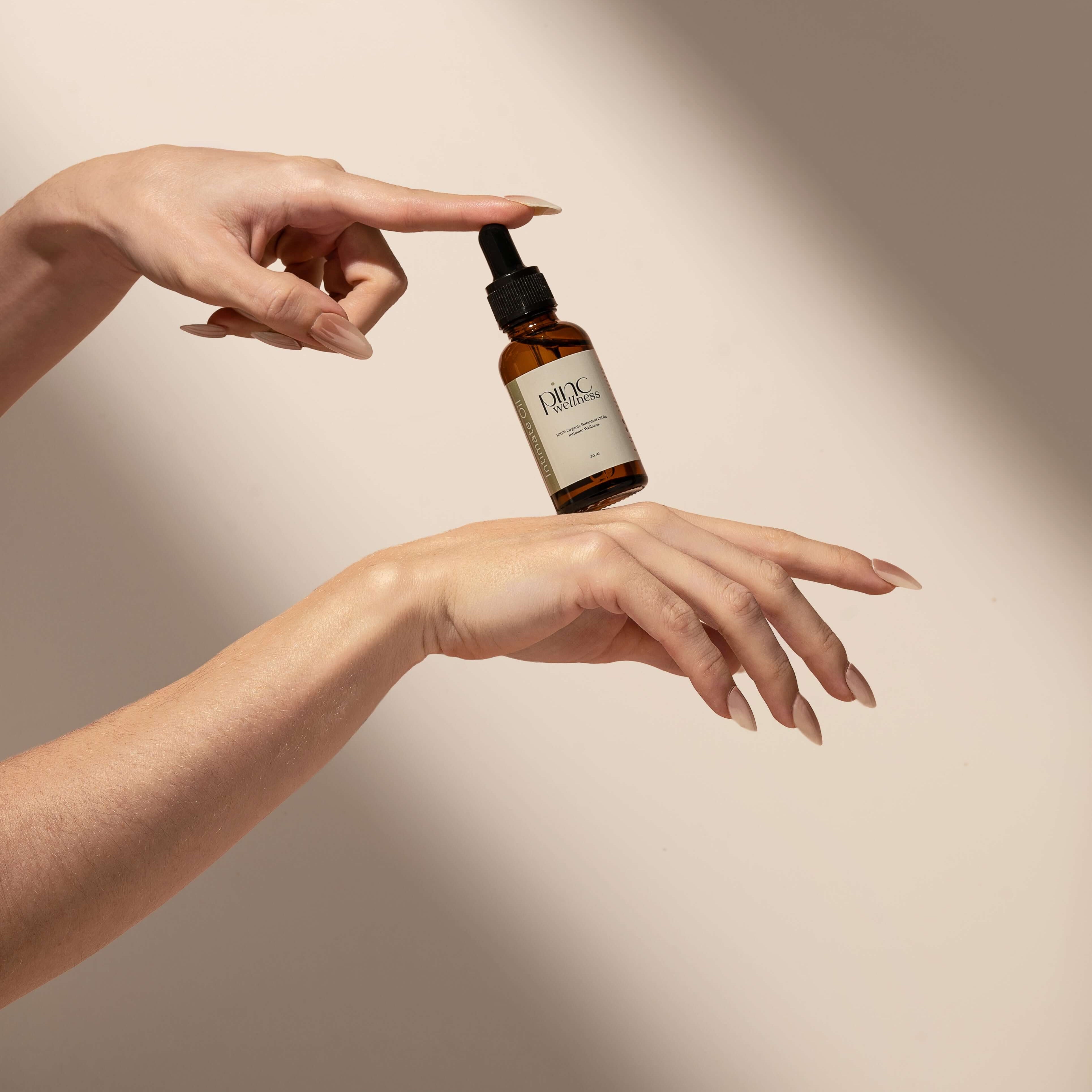 Person in beige underwear holding dropper above brown "Pinc Wellness" bottle.