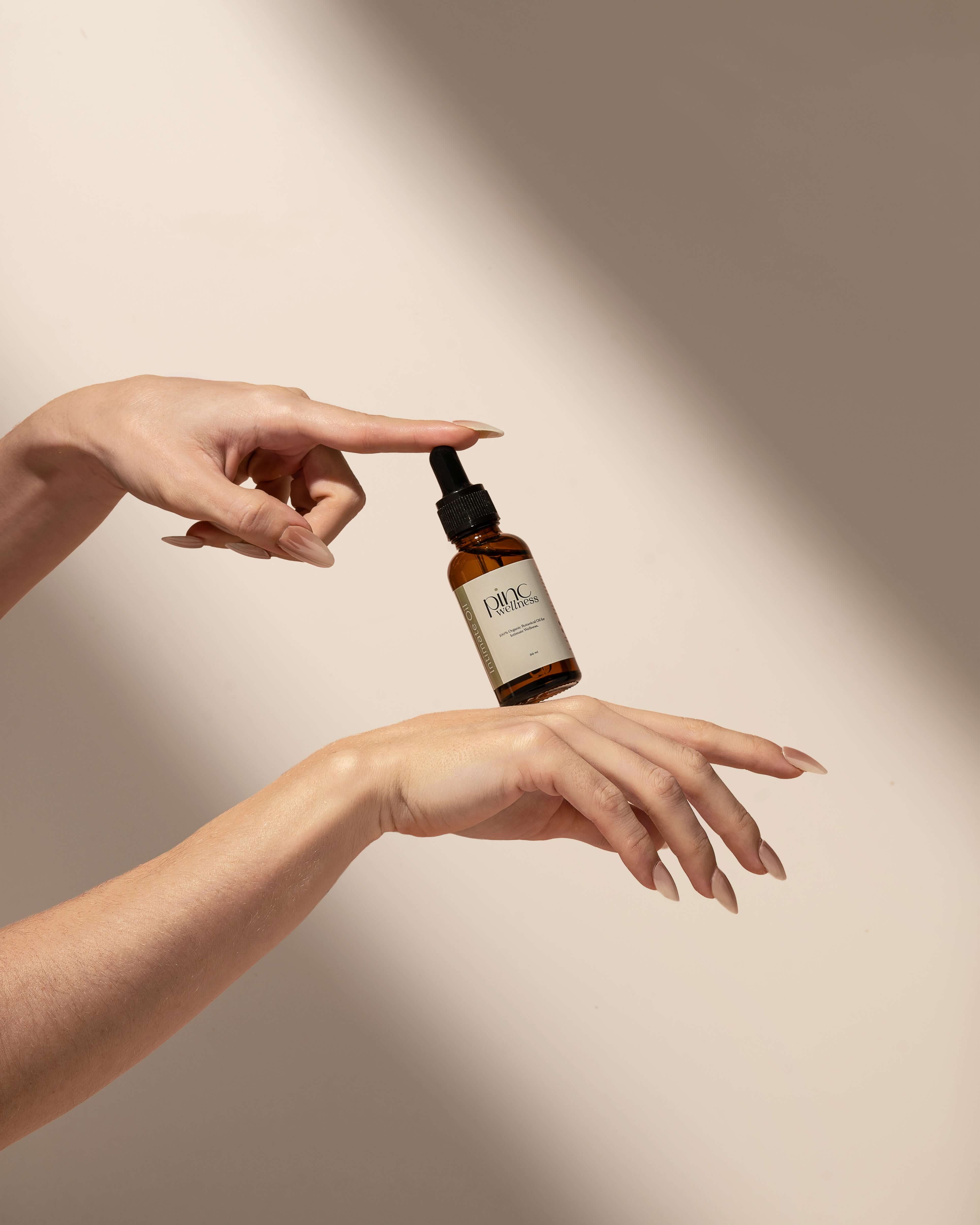 Person in beige underwear holding dropper above brown "Pinc Wellness" bottle.
