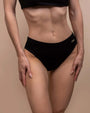 Close-up of toned midriff in black underwear, neutral background, confident.