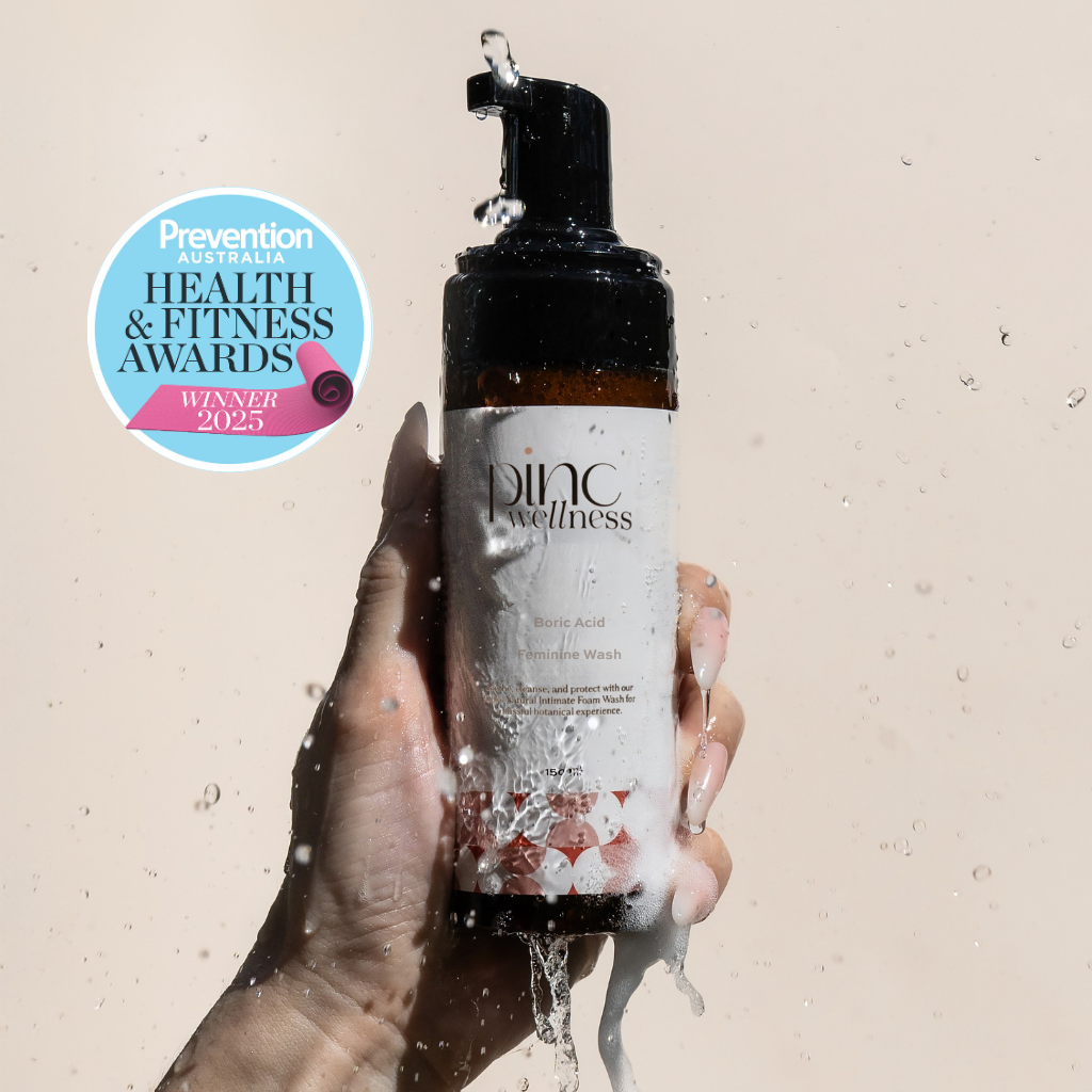 Hand holding a bottle of 'Pinc Wellness' product with a Prevention Australia Health & Fitness Award badge on a beige background.