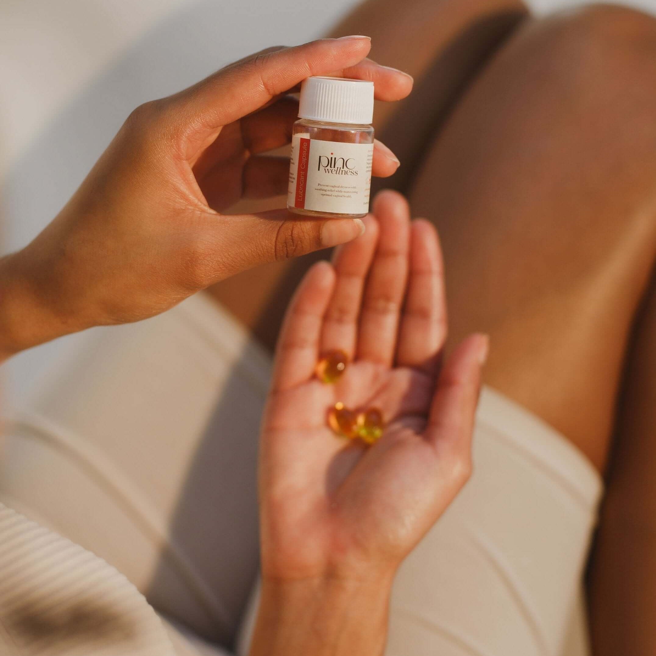 Person holding lubricant capsules bottle with capsules in hand for intimate hydration and comfort.