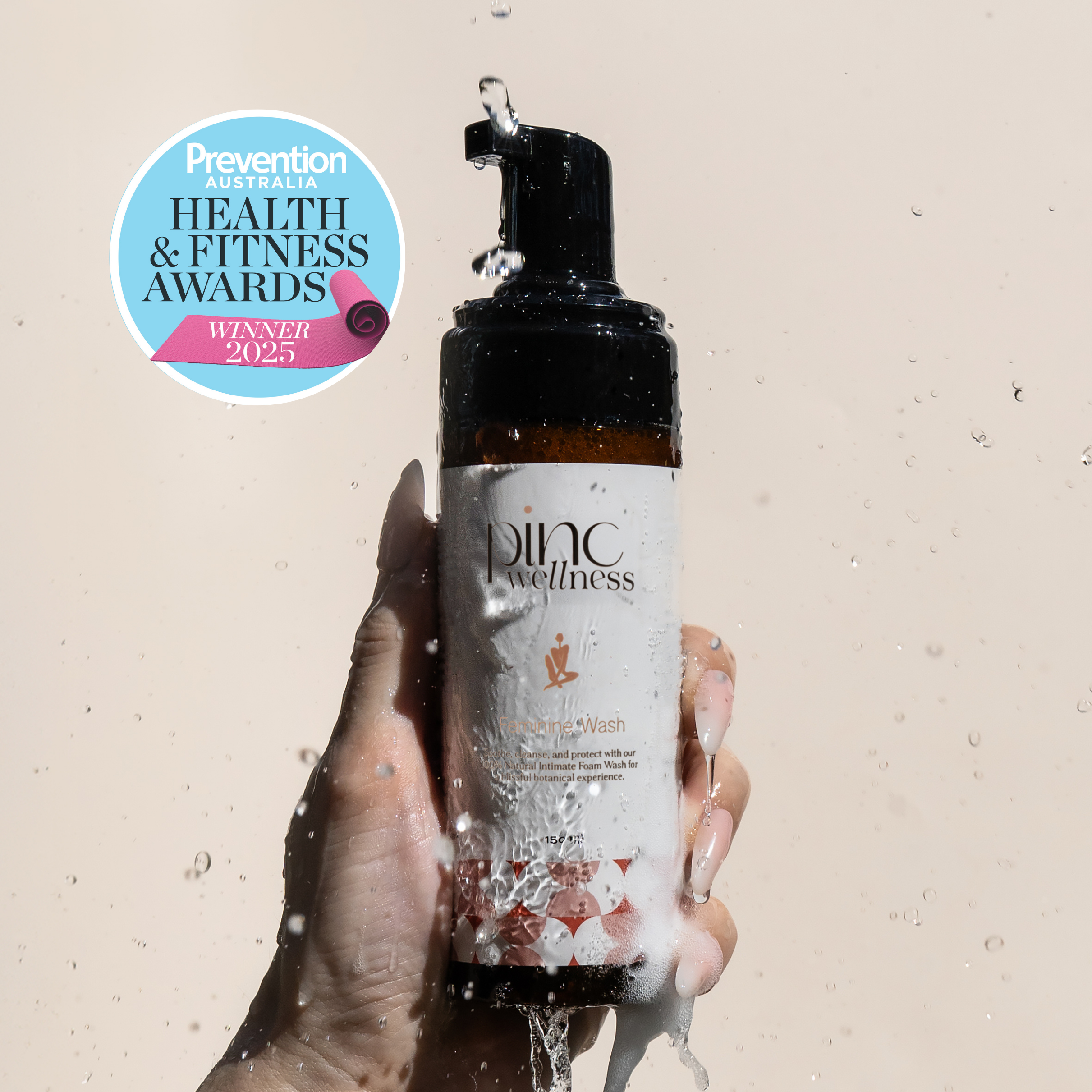 Hand holding a bottle of 'Pinc Wellness' product with a Prevention Health & Fitness Awards logo on a beige background.