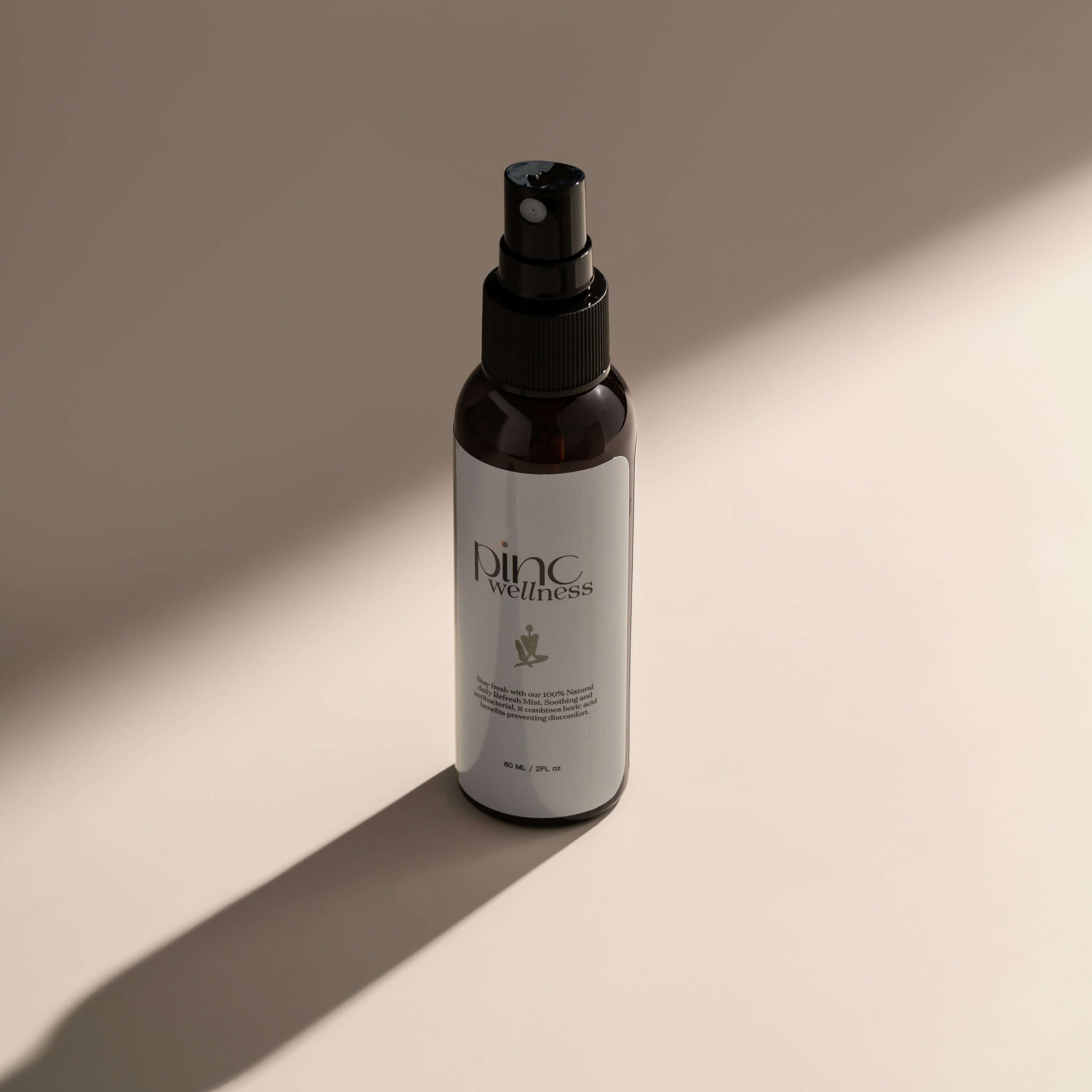 Dark Pinc Wellness spray bottle on light surface, long shadow, minimalist.