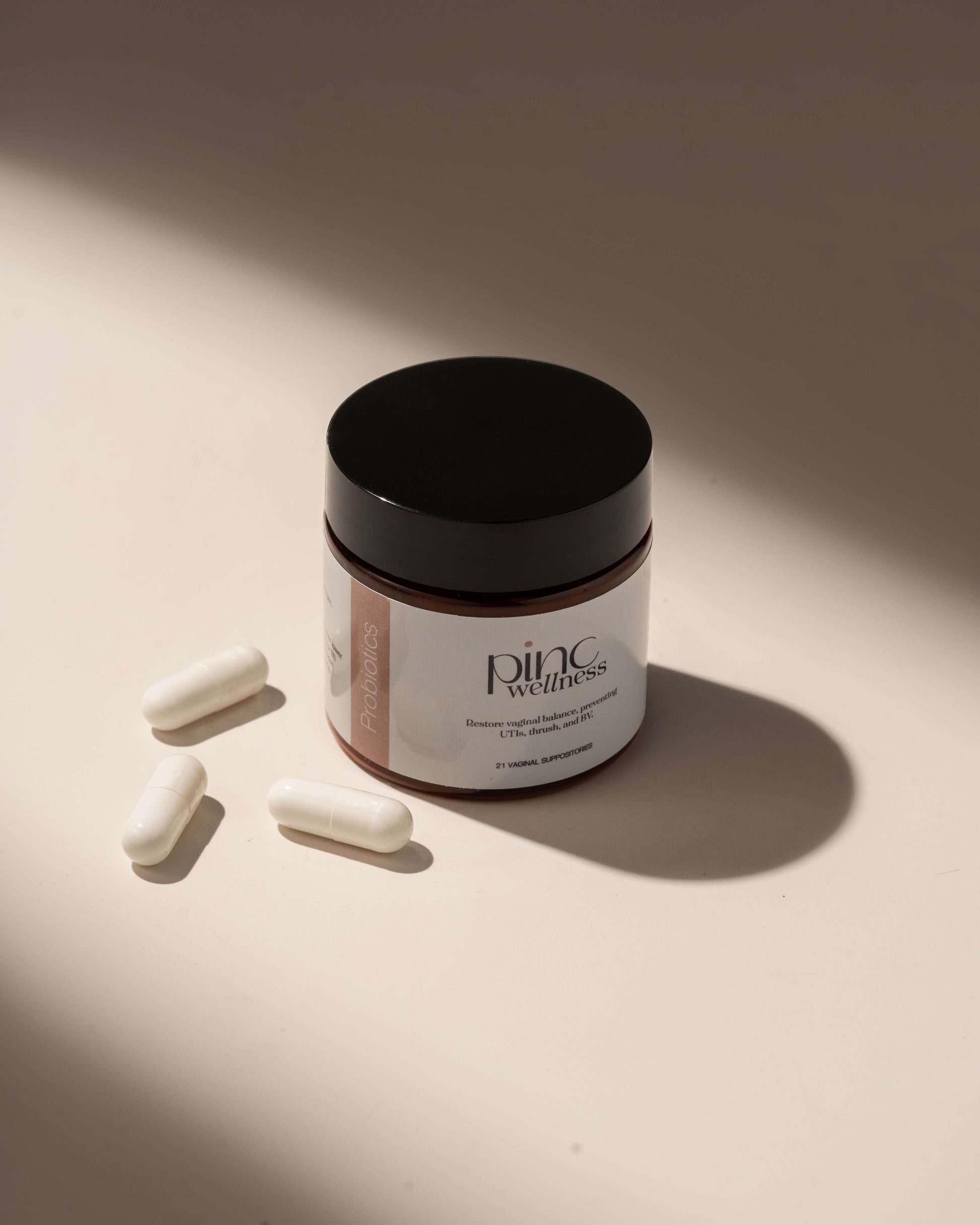 Small Pinc Wellness jar with black lid, four capsules on light surface.