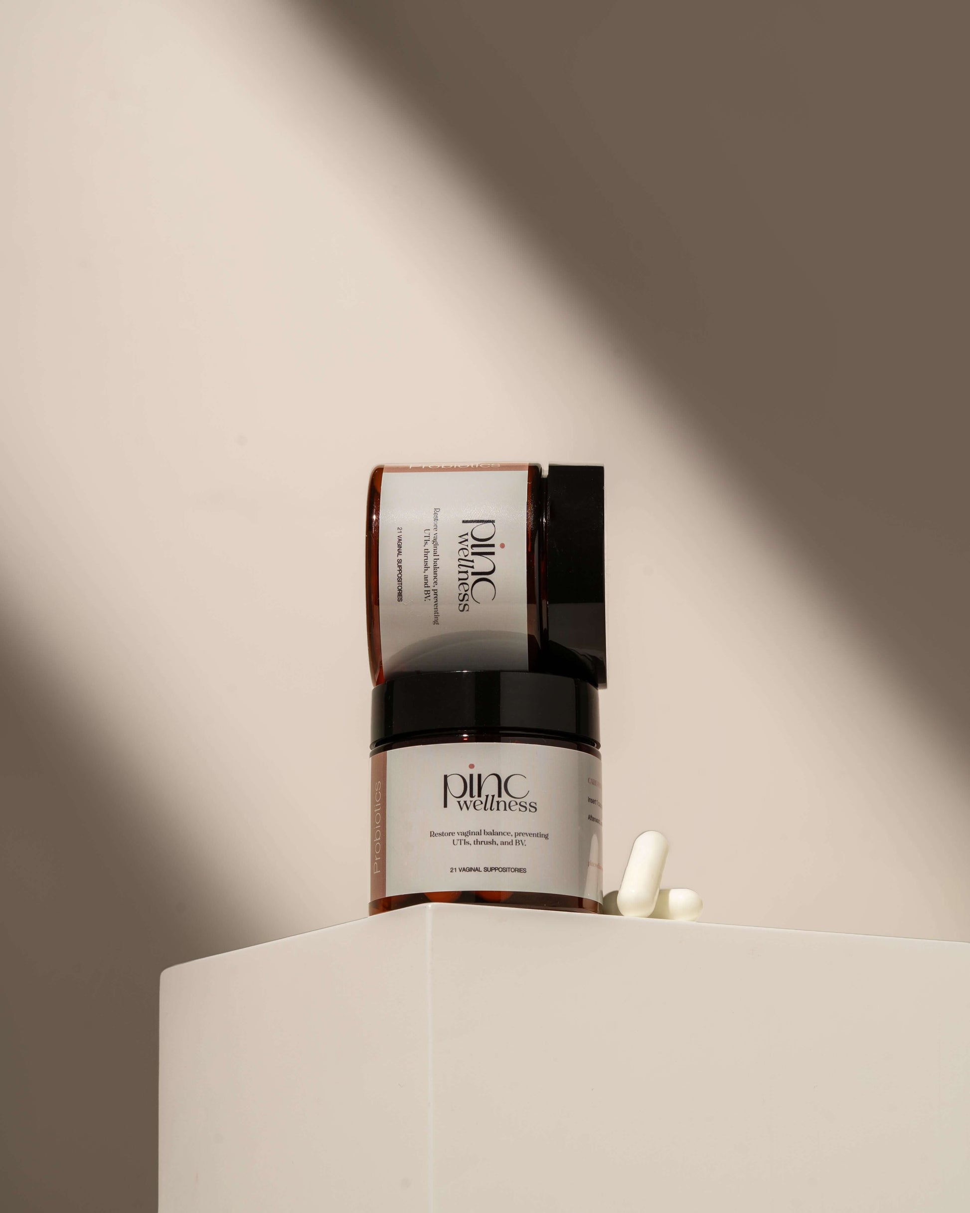 Jar and box of Pinc Wellness supplements on white pedestal with capsules.